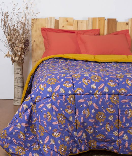 Couverture piquée en laine à motif floral rose et bleu sur un lit, avec revers jaune moutarde rabattu.